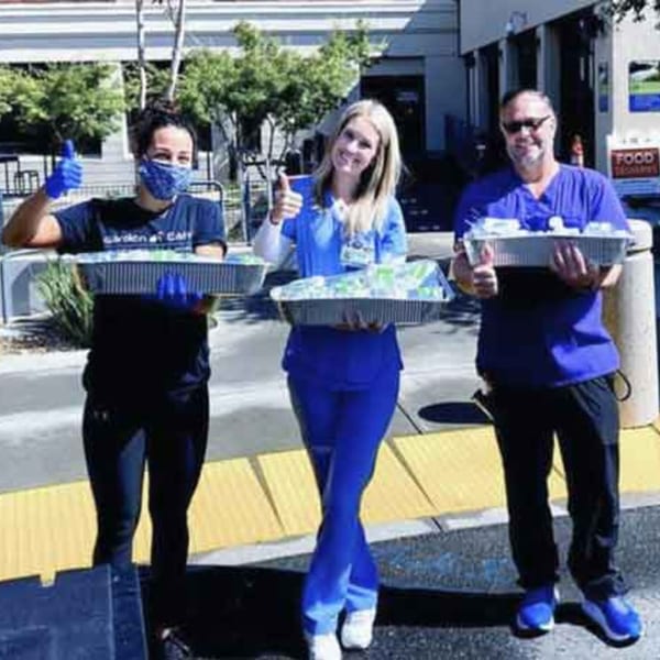 Three Garden of Eat'n staff members, two women and one man, holding catering trays and giving thumbs up.