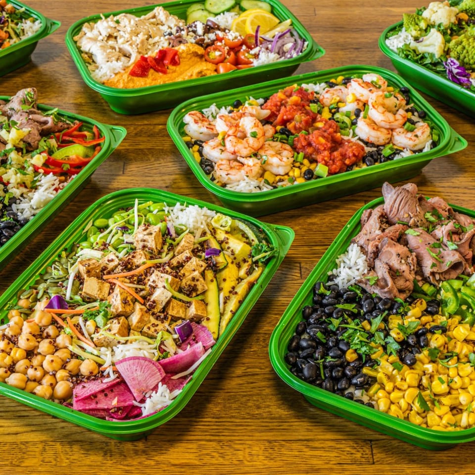 Several vibrant Garden of Eat'n healthy bowls with various proteins and fresh ingredients on a wooden table.