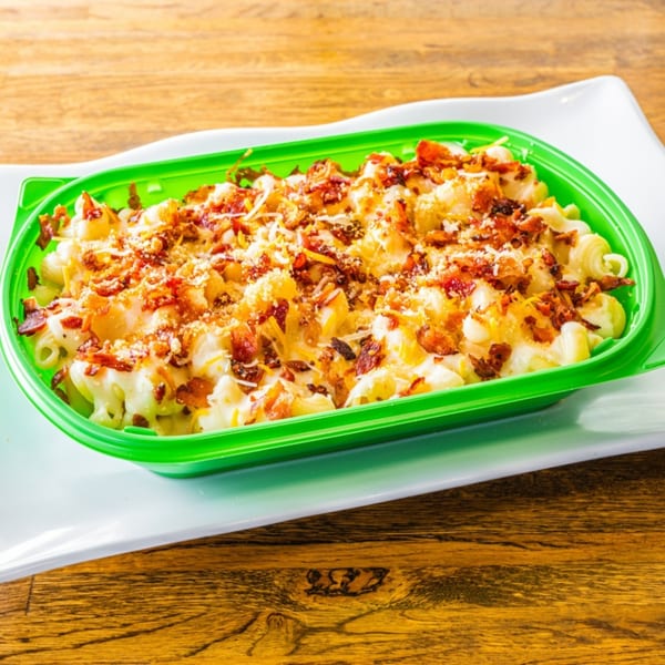 Macaroni and cheese topped with bacon bits and shredded cheese in a bright green container.