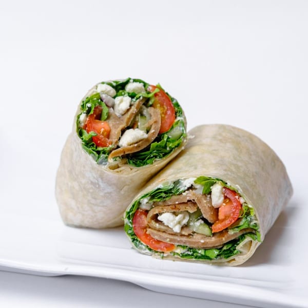 Two halves of a healthy wrap filled with lettuce, tomatoes, feta, and meat on a white plate.