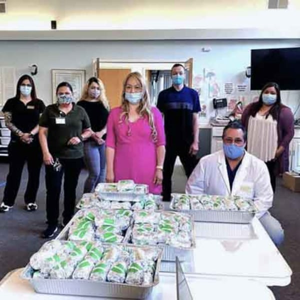 Garden of Eat'n staff in masks with trays of healthy wrapped meals for catering.