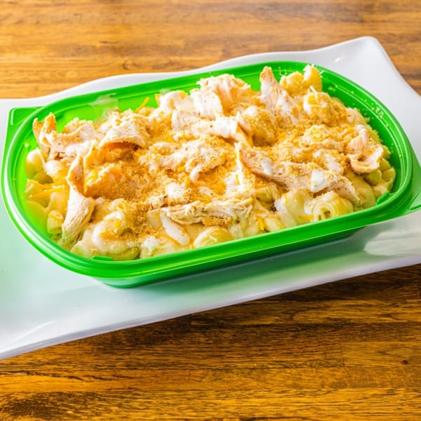 Mac and cheese with shredded chicken and breadcrumbs in a bright green container on a white plate.