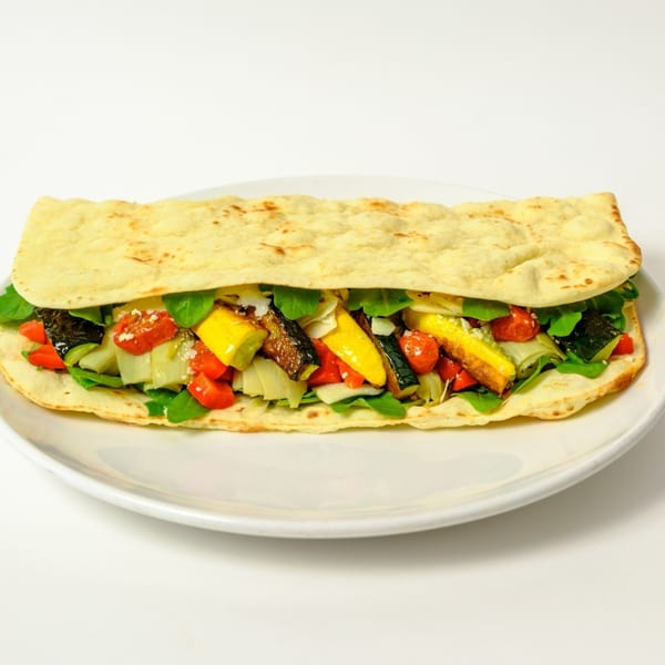 A Garden of Eat'n flatbread sandwich filled with colorful roasted vegetables and greens on a white plate.