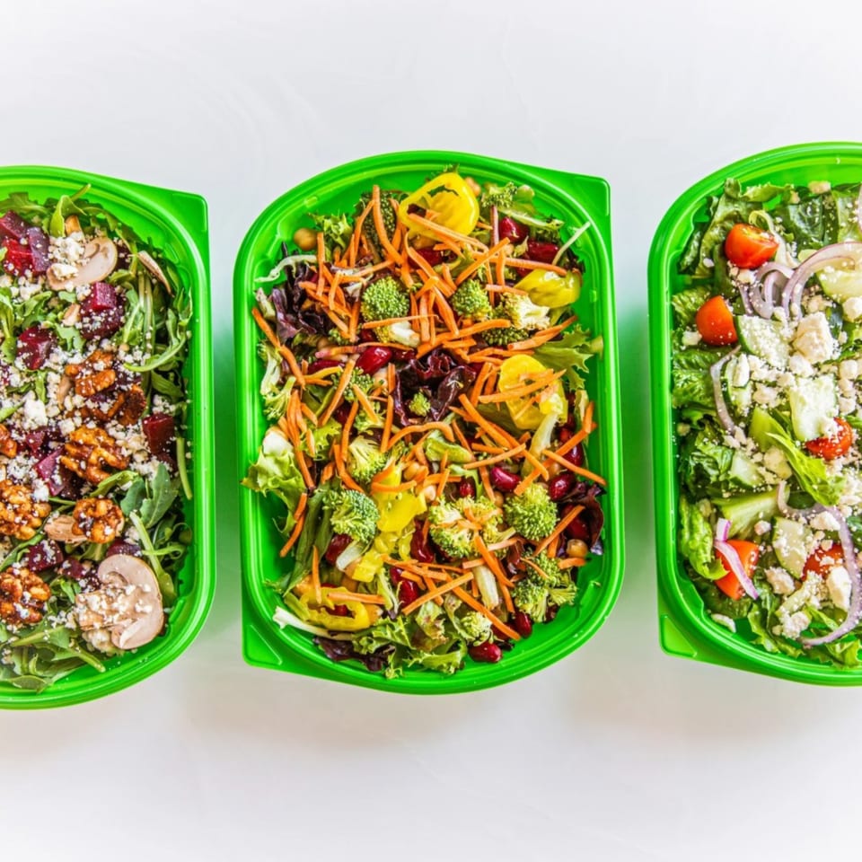 Three vibrant salads in green containers, featuring fresh vegetables, nuts, and cheese, from Garden of Eat'n.