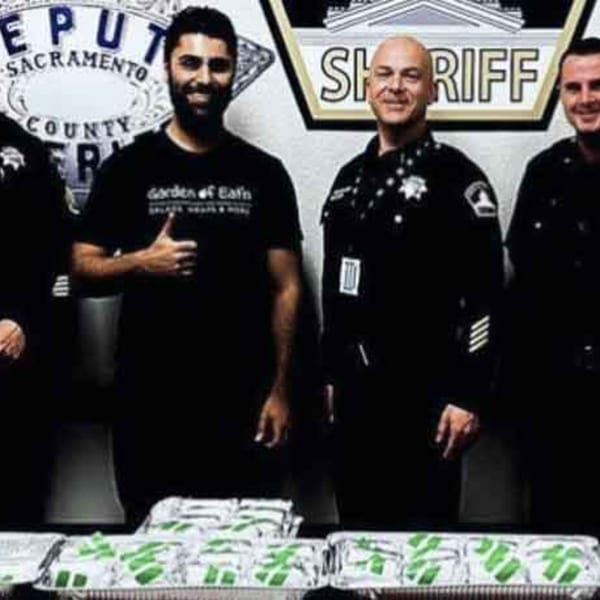 A Garden of Eat'n employee and three police officers stand behind several trays of food.