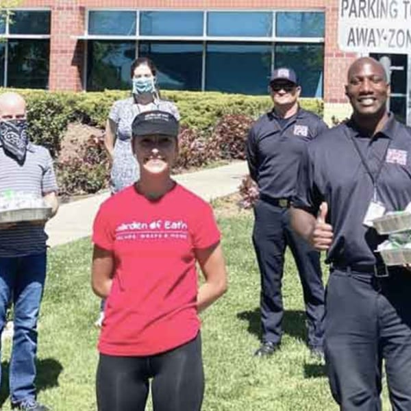 Garden of Eat'n staff and community members outdoors, holding food containers, smiling.